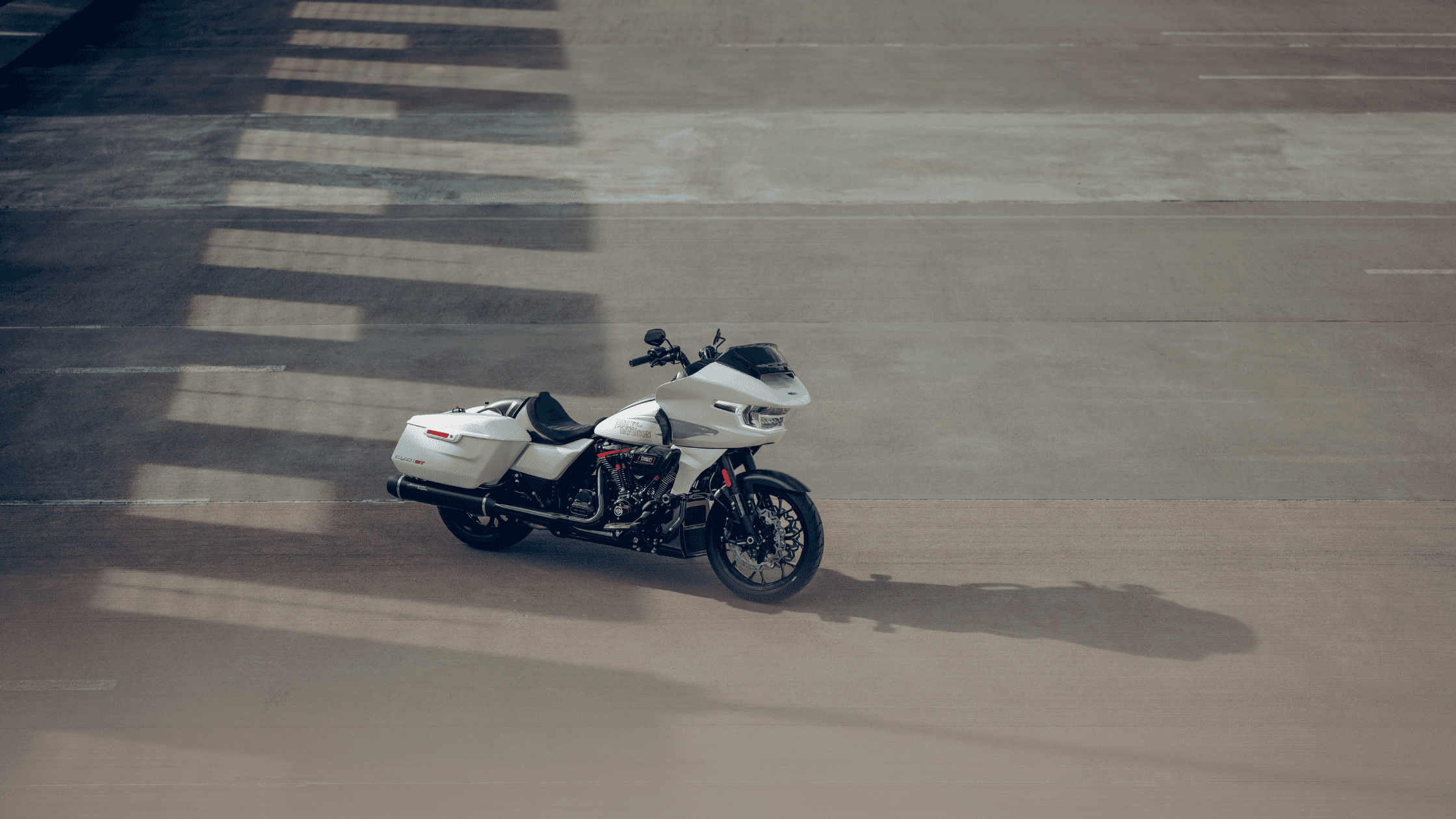 A white motorcycle parked on an empty concrete lot with shadows of overhangs falling across the ground.