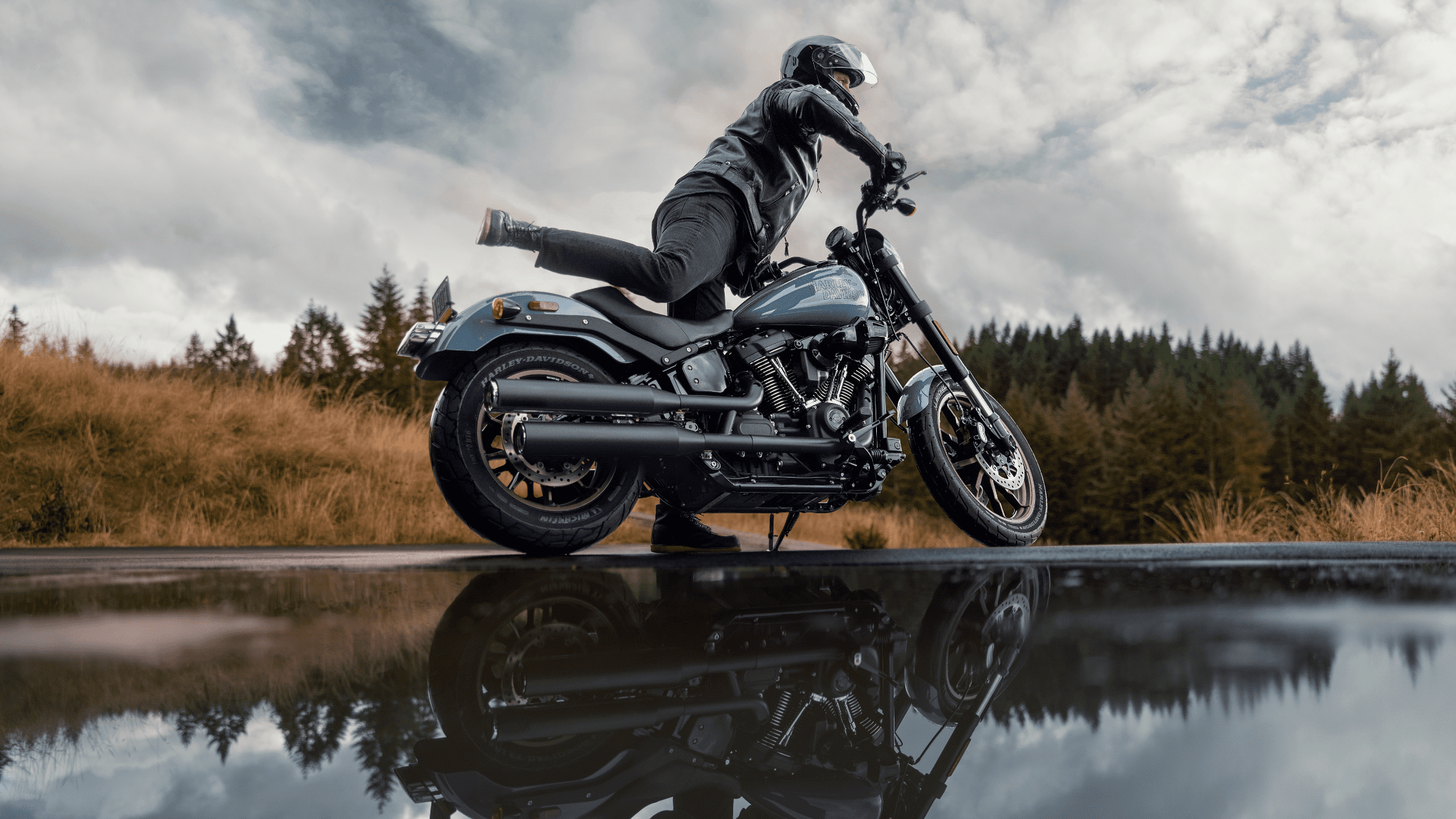 A rider mounting the 2024 Harley-Davidson® Low Rider® S near Covington, GA, set against a scenic backdrop of nature, showcasing the bike's powerful build and agility.