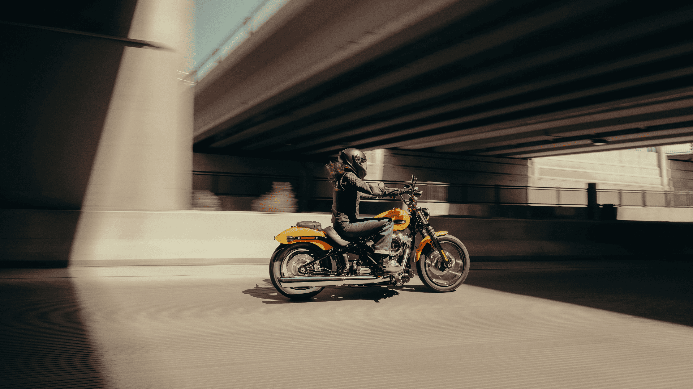 Woman riding a 2025 Harley-Davidson® Street Bob® through Covington, GA, with a low-slung stance and bright orange tank under urban overpass.